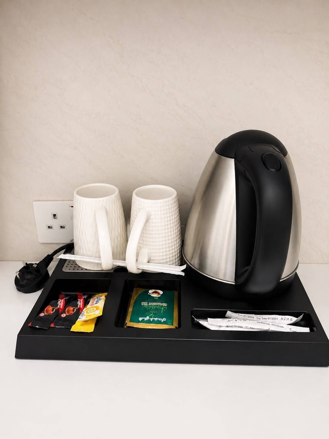 Una cafetera, dos tazas, una caja de pañuelos, un sobre de té y una bandeja con cable de alimentación.