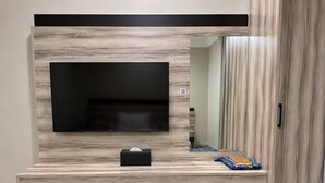 A hotel room with a flat-screen TV mounted on a wooden wall, a small bedside table with a tissue box, a trash bin, and a wardrobe. - Tallaq hotel (Madinah)