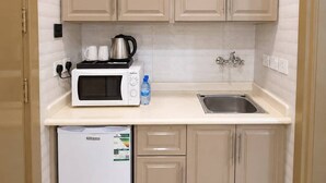 A compact kitchen with beige cabinets, a microwave, a kettle, and a refrigerator. - Tallaq hotel (Madinah)