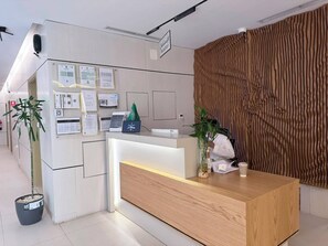 A reception desk with a wooden finish, a digital screen, and various informational posters on the wall.