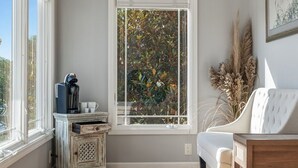 Una habitació amb un finestral gran, un sofà blanc, una taula de fusta i un moble decoratiu.