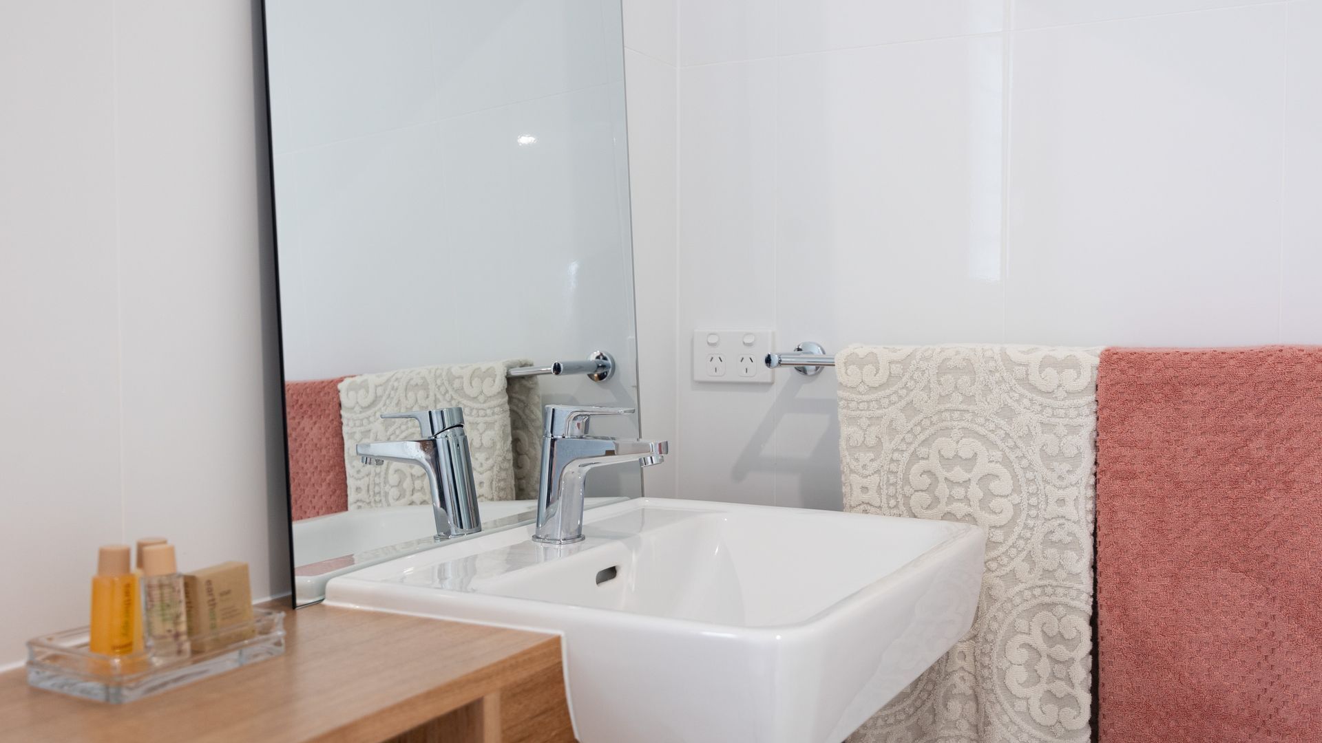 Un bagno con un lavandino bianco, due rubinetti e uno specchio. Ci sono articoli da toilette sul ripiano.