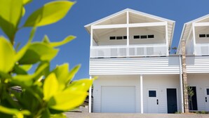 A two-story building with a balcony on the upper floor, a garage on the ground floor, and a clear blue sky in the background. - Igloo - Whole House in Mollymook (Mollymook)