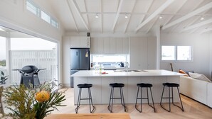 A modern kitchen with a large island, bar stools, and a built-in refrigerator. - Igloo - Whole House in Mollymook (Mollymook)