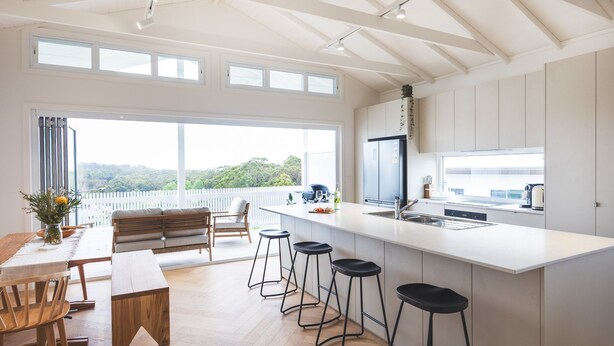 A modern kitchen with a large island, bar stools, and a dining area with a wooden table and chairs. - Igloo - Whole House in Mollymook (Mollymook)