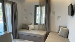A modern room with a sofa bed, a small table, and a TV mounted on the wall. - Latramys Suites (Naxos)