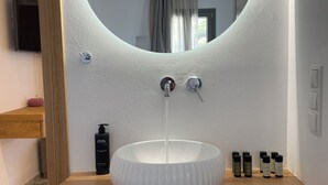 A bathroom with a round mirror, a white sink, and a wooden countertop. - Latramys Suites (Naxos)