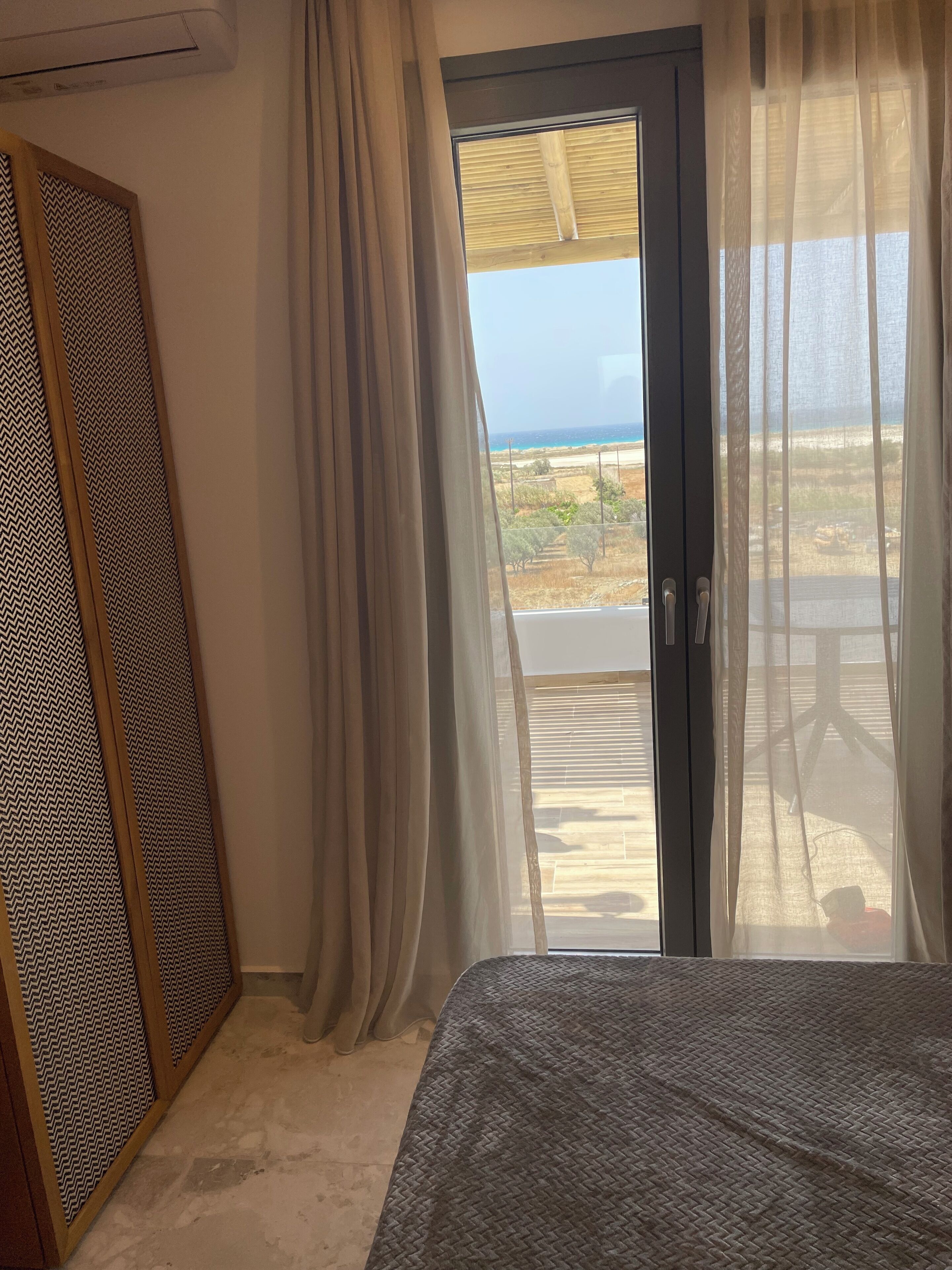 Quarto com cama, porta de correr de vidro para uma varanda e vista para o mar.