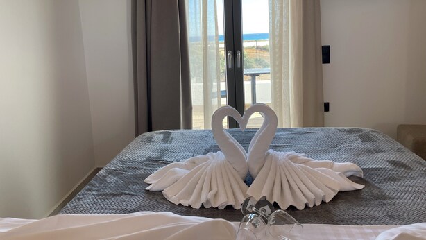 A hotel room with a bed, a TV mounted on the wall, and a view of the sea through the window. - Latramys Suites (Naxos)