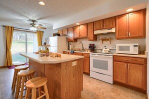 A kitchen with wooden cabinets, a central island with stools, a microwave, an oven, and a ceiling fan. - Ranch retreat in the heart of Hocking Hills (South Bloomingville)