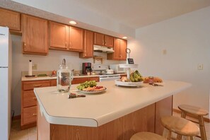 A modern kitchen with wooden cabinets, a white countertop, and a central island with a fruit display.