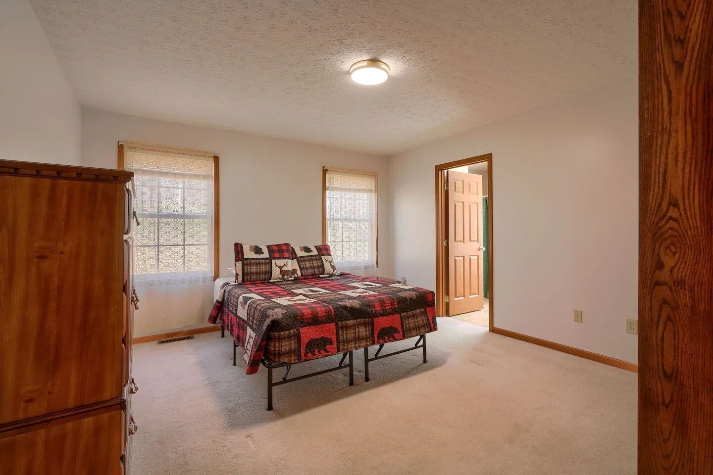 A bedroom with a bed, a wooden wardrobe, and a door leading to another room.