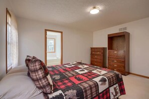 A bedroom with a bed, a wooden dresser, and a door leading to another room.