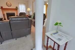A living room with a leather sofa, a fireplace, a clock, and a welcome sign on a table.