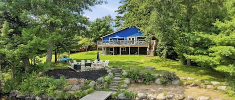 A lakeside cabin with a deck, outdoor seating, and a stone pathway leading to a dock.