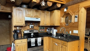 A wooden cabin kitchen with a stove, sink, and wooden cabinets. - Your Perfect Mountain Escape-Cozy Cabin Retreat. (Errol)