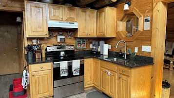 A wooden cabin kitchen with a stove, sink, and wooden cabinets.