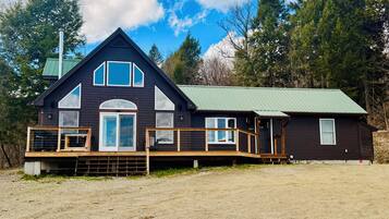 A two-story house with a green roof, a front porch, and a fenced deck area.