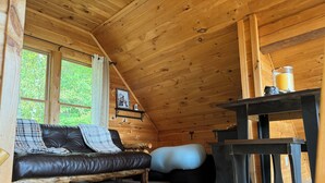 A cozy cabin interior with a leather sofa, a bean bag, a wooden table, and a window with a view of greenery. - Your Perfect Mountain Escape-Cozy Cabin Retreat. (Errol)
