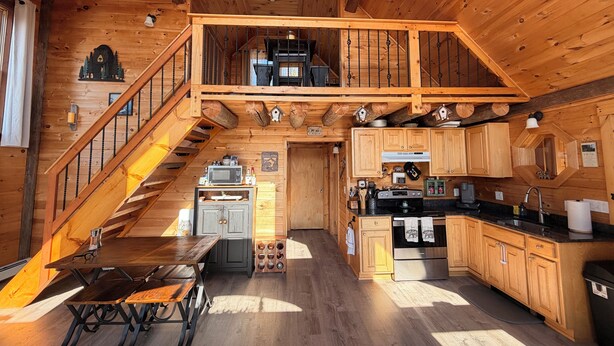 A wooden cabin with a kitchen, dining area, and a staircase leading to a loft. - Your Perfect Mountain Escape-Cozy Cabin Retreat. (Errol)