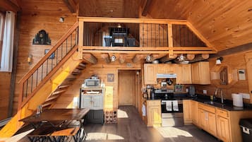 A wooden cabin with a kitchen, dining area, and a staircase leading to a loft.