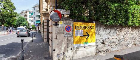 Una esquina de calle con un letrero amarillo que dice 'INGRESSO', una señal de no estacionamiento y un letrero que indica 'Via Roma'.