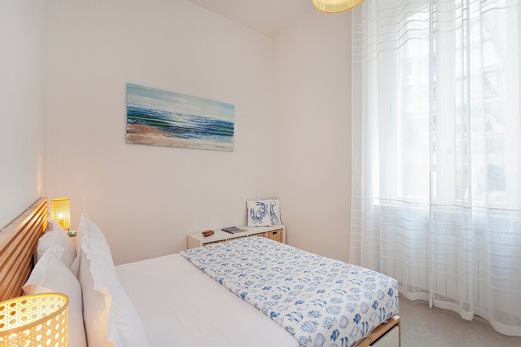 A bedroom with a bed, a painting, a nightstand, and a lamp.