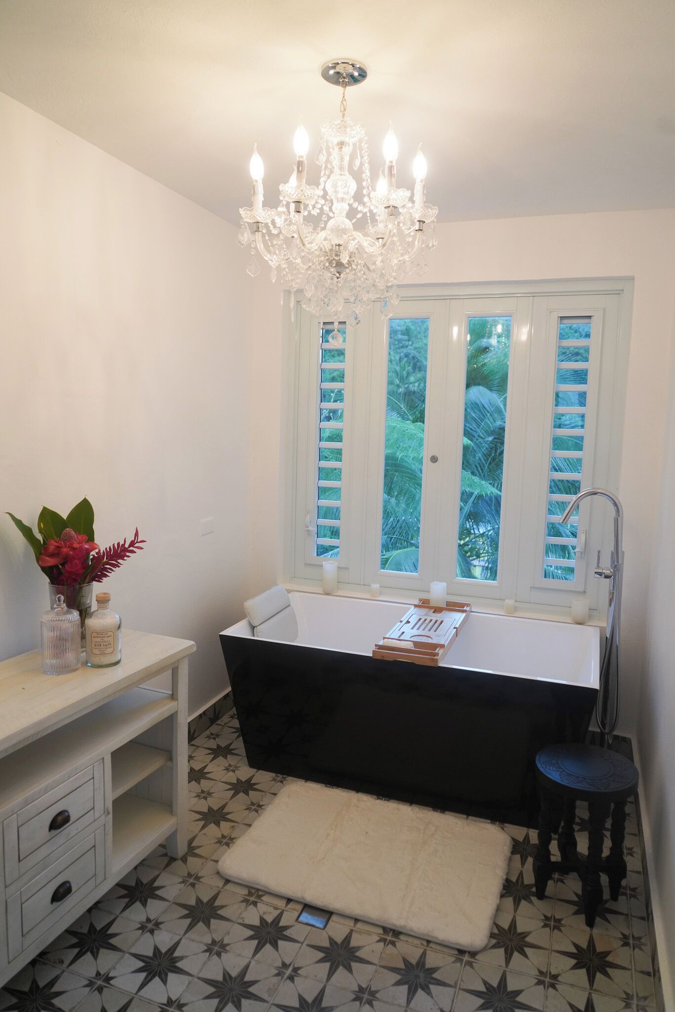 Un baño con bañera, un candelabro, una ventana con contraventanas y un suelo con diseño de estrellas.