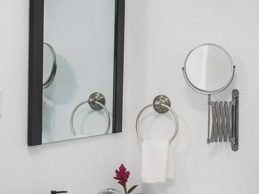 Un baño con lavamanos blanco, un espejo, argolla para toallas, secamanos automático y dispensador de jabón.