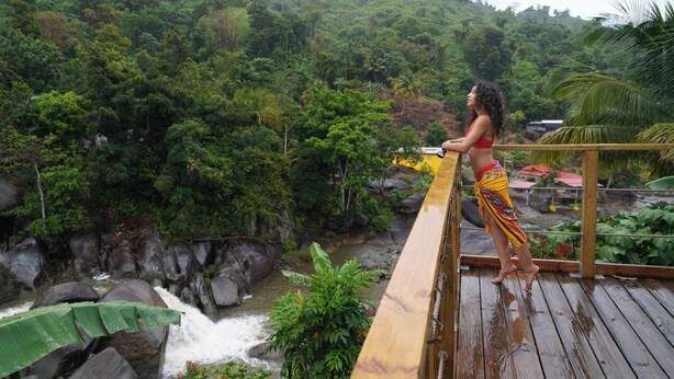 A person standing on a wooden deck overlooking a waterfall and lush greenery. - El Yunque Rainforest (Naguabo)