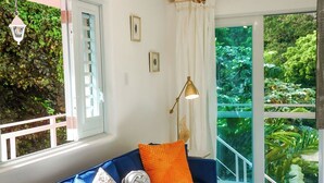 A modern living room with a blue sofa, a patterned rug, and a view of lush greenery through large windows. - El Yunque Rainforest (Naguabo)