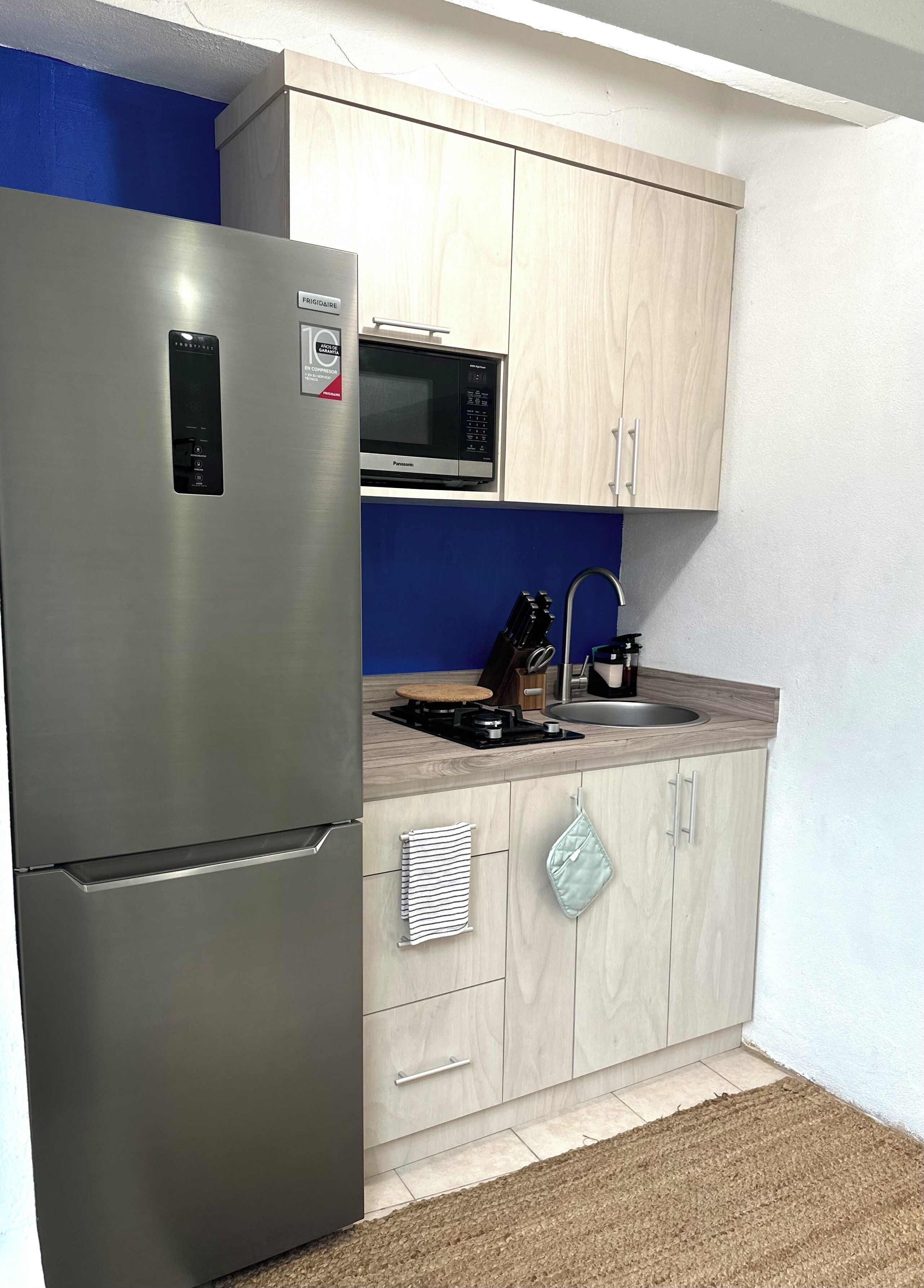 A compact kitchen with a stainless steel refrigerator, a microwave, and a sink with a faucet.