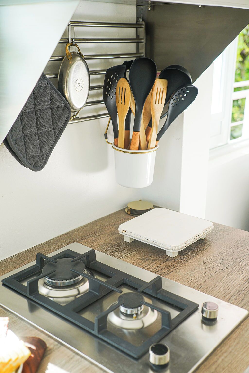 A kitchen with a gas stove, a hanging pot rack, and a utensil holder.