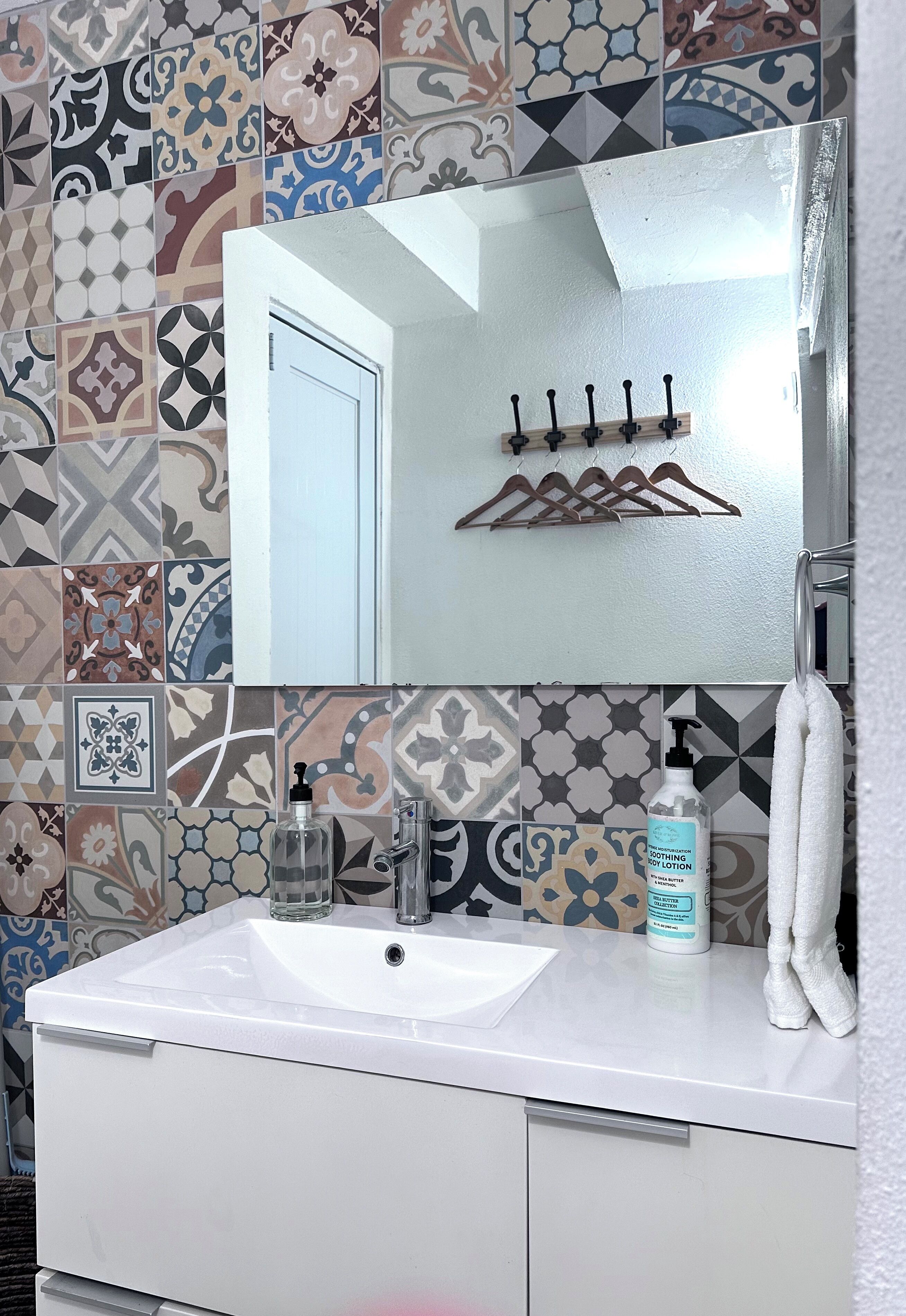 A bathroom with a white sink, a mirror, a towel rack, and a bottle of lotion.