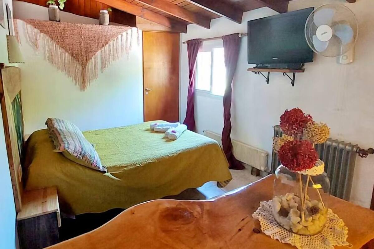 Een kamer met een bed, een houten tafel met een decoratief object, een televisie en een radiator.