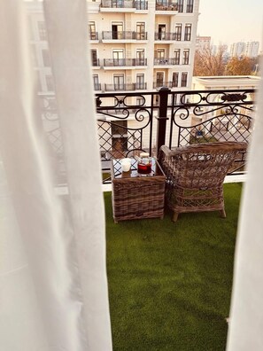 A balcony with wicker furniture and a small table, overlooking a residential area.
