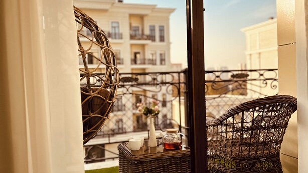 A balcony with wicker furniture, a small table with a vase and a bottle, and a view of a building across the street. - Tashkent City Boulevard (Tashkent)