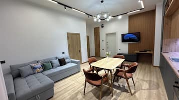 Una sala de estar moderna con un sofá gris, una mesa de comedor de madera y un televisor montado en la pared.
