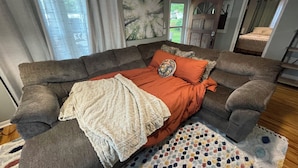 Un salon avec un canapé d’angle, un tapis à motifs et une porte donnant sur une autre pièce.