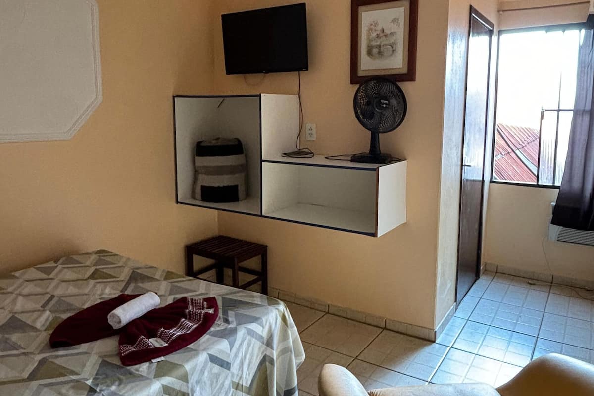 A hotel room with a bed, a chair, a TV, a small table, and a window.