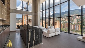 A modern kitchen with a marble island, a dining area with white sofas, and large windows offering a city view.
