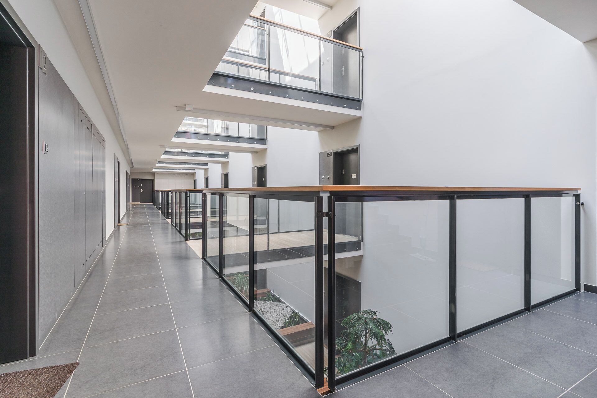 A modern interior with a glass railing, a long corridor, and a high ceiling with skylights.