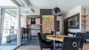 A modern kitchen with a dining area, a large window, and a colorful abstract painting. - Scala Premium by Grand Apartments (Gdansk)