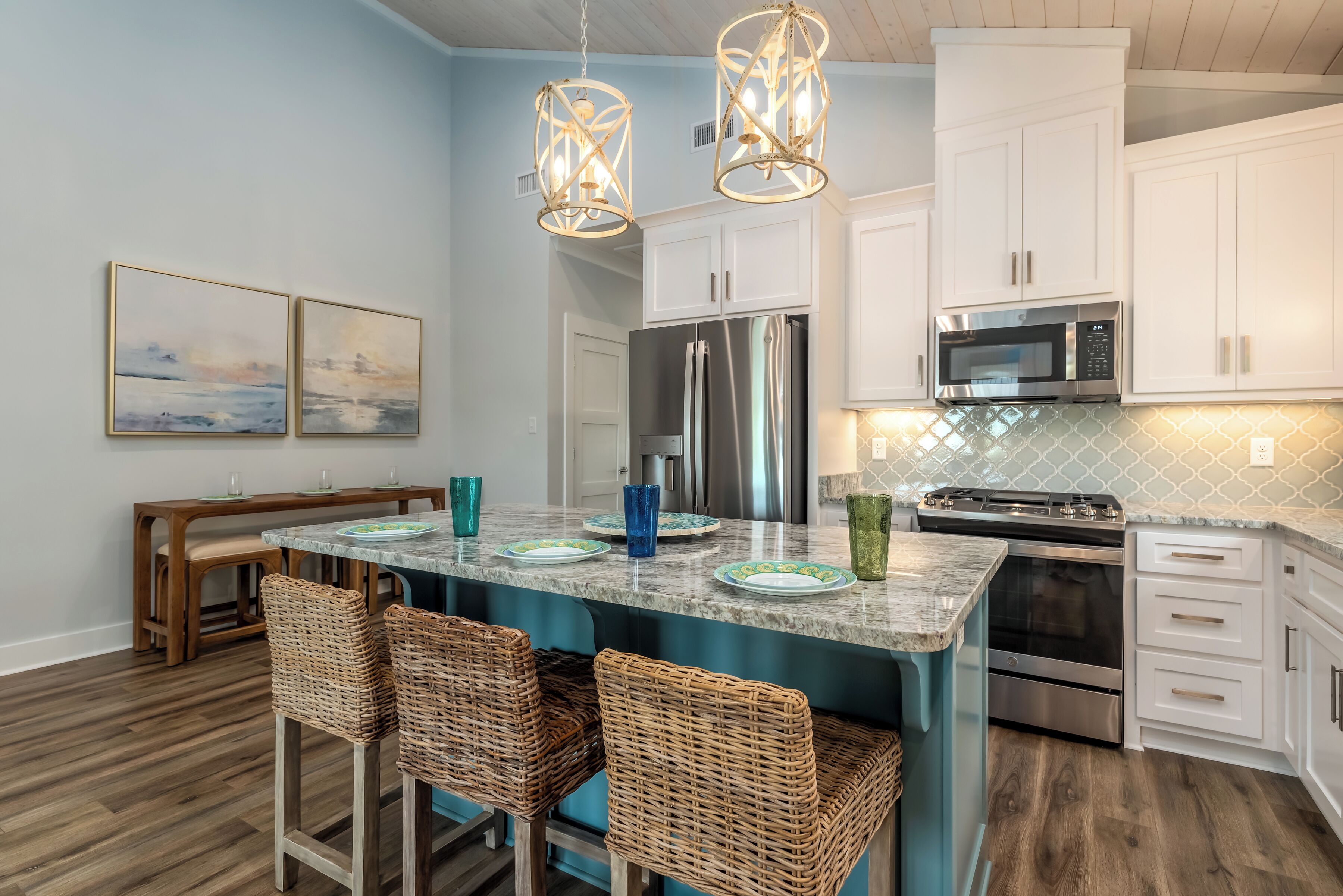 A modern kitchen with white cabinets, stainless steel appliances, and a teal island with bar stools.