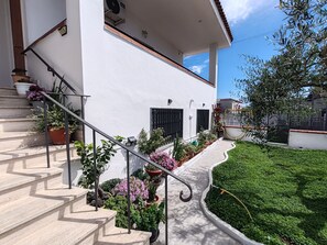 Um edifício branco com escadaria, vasos de plantas e um jardim bem cuidado.