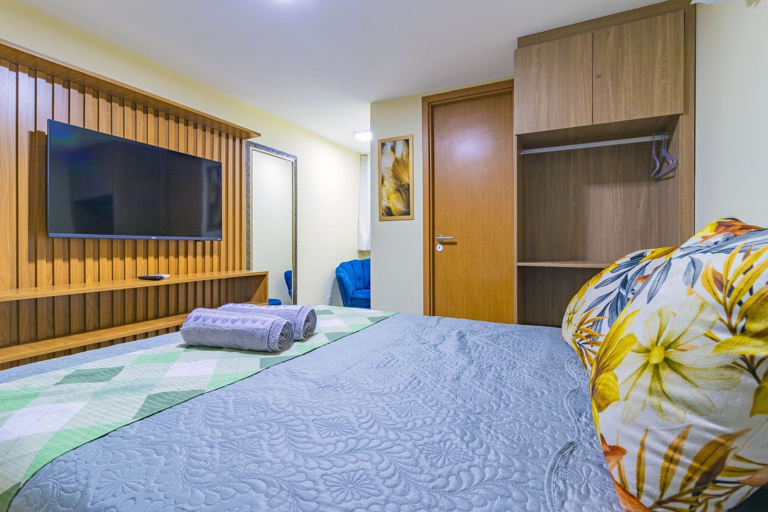 A bedroom with a bed, a television, a wardrobe, and a painting on the wall.