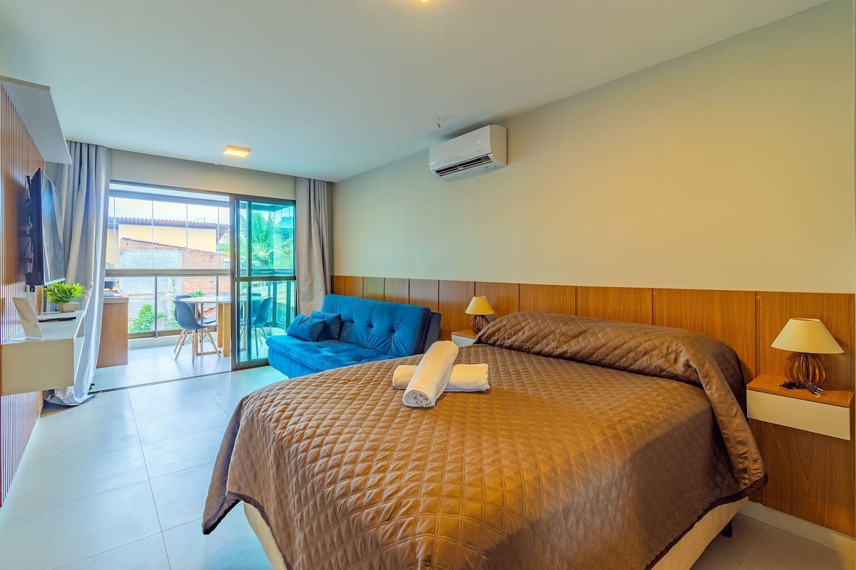 A hotel room with a large bed, a desk, a chair, and a view of the outside.