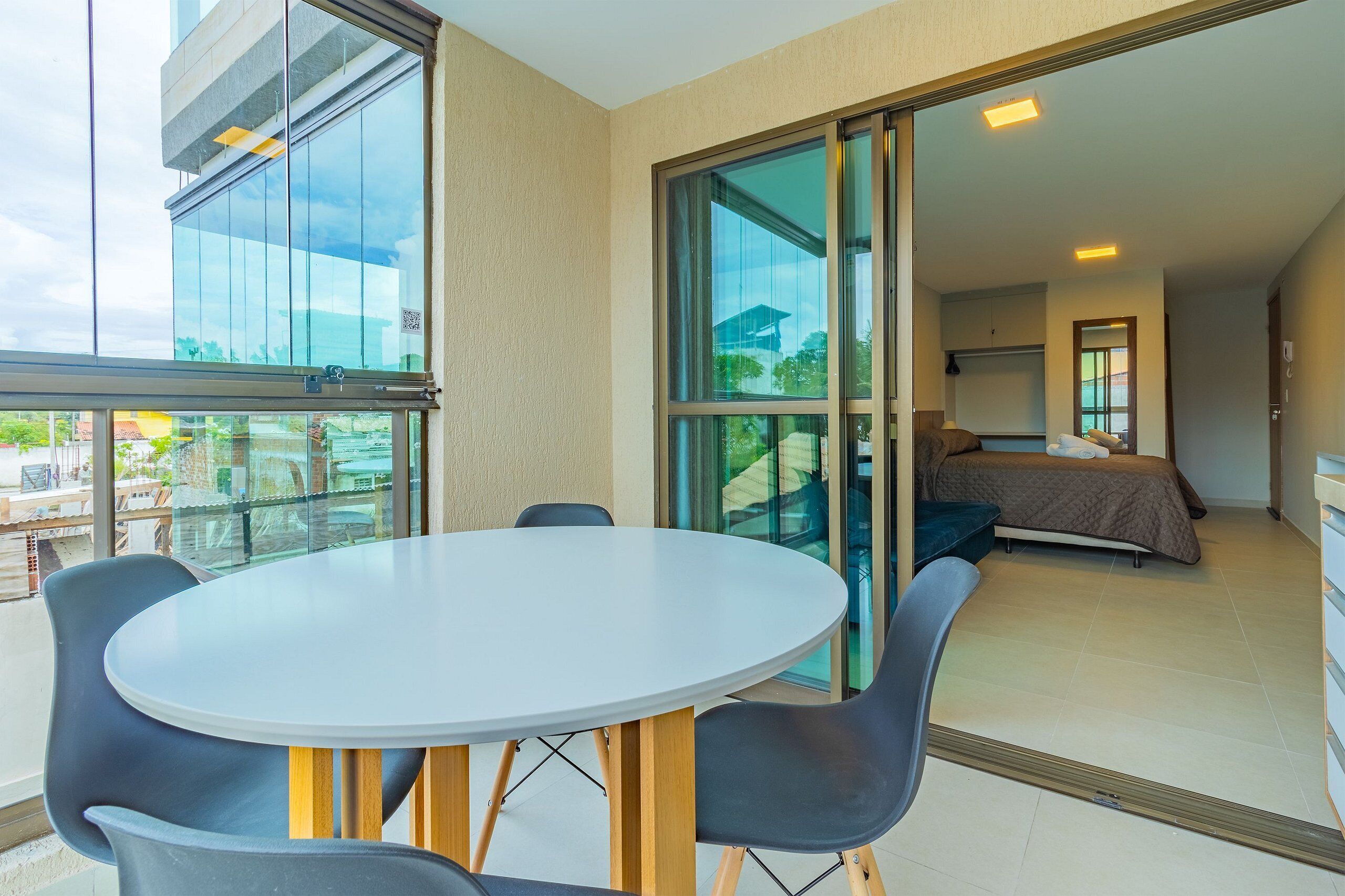 A modern hotel room with a balcony, a round table with chairs, a bed, and a large window.