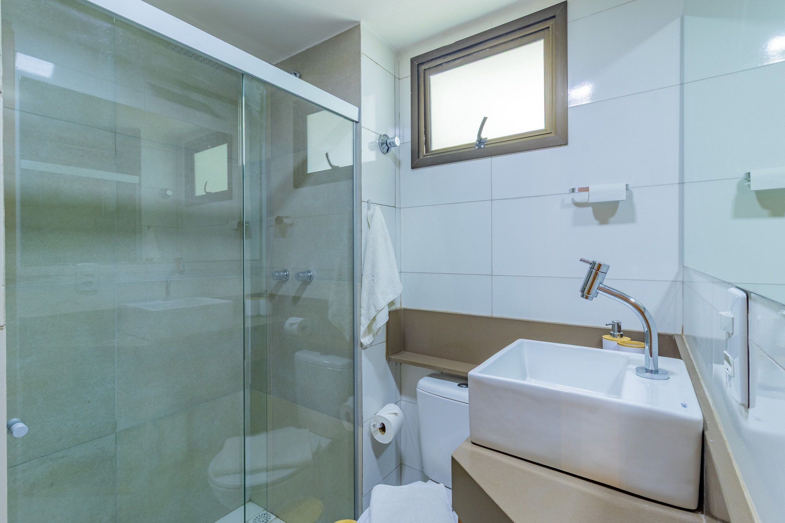 Un baño con cabina de ducha de vidrio, un lavamanos blanco, un inodoro y un espejo.