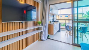 Un salon moderne doté d’un téléviseur à écran plat, d’un mur avec des lambris en bois et d’une porte-fenêtre coulissante donnant sur un balcon aménagé avec des sièges d’extérieur.